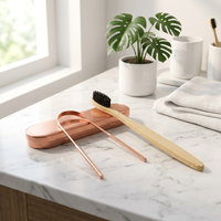 Eco oral care duo bundle featuring bamboo toothbrush and copper tongue scraper on natural marble surface with monstera plant